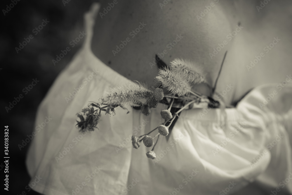 Obraz premium Delicate bouquet of wildflowers in the neckline on the naked shoulder of an attractive woman in a white blouse. Romance and peace with a loved one
