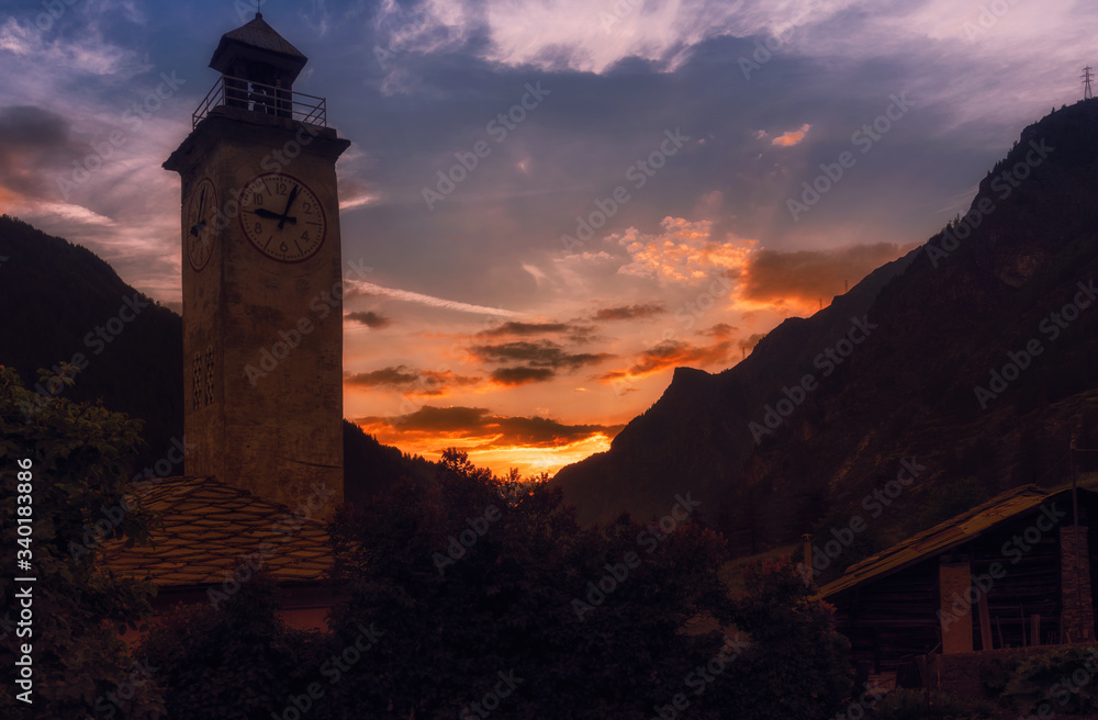 The bell tower and the old alpine village illuminated by the warm reflections of the sunset