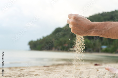 Play with sand on the beach. Sand is poured from the hands, against the backdrop of a tropical island.