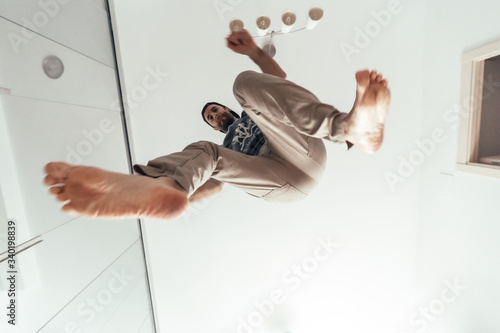 A young man doing parkour from home, photographed from below and looking at camera