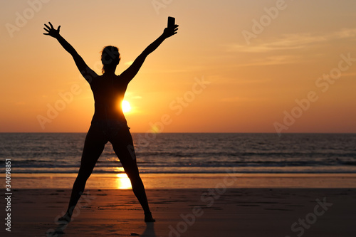A young happy woman celebrating the end of lock down, on the beach at sunset after the coronavirus pandemic