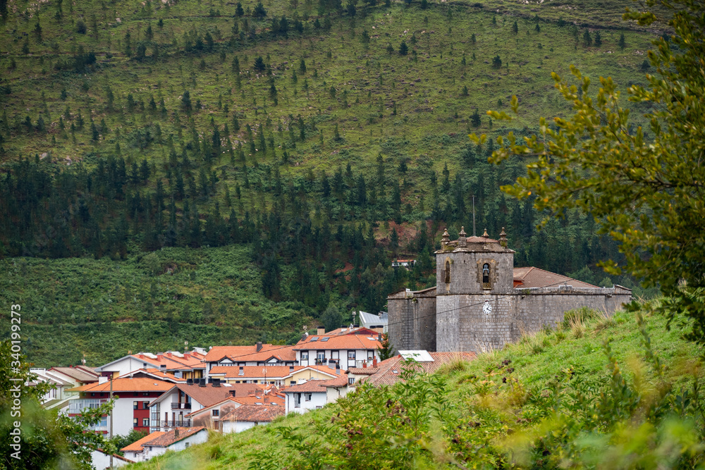 Old traditional houses at the village with medieval church and green mountains. Typical rural village in the mountains of Basque Country, Spain. Camino de Santiago.