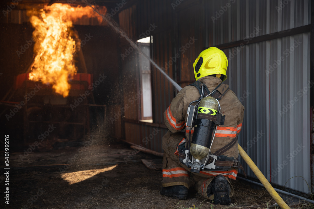 Obraz premium Rear view of Fireman wear fire protection suit walking into the fire training room and Spray water Fire at fire station. Training fire drill Concept.
