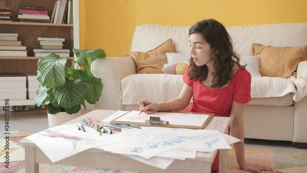 Portrait of a Young Beautiful Artist Girl with Braces. Attractive Woman Sitting on a Floor and Draws a Picture with Colored Pencils. Cozy Home interior, Yellow Wall, House Plants. Portrait of a Young Beautiful Artist Girl with Braces. Attractive Woman Sitting on a Floor and Draws a Picture with Colored Pencils. Cozy Home interior, Yellow Wall, House Plants.