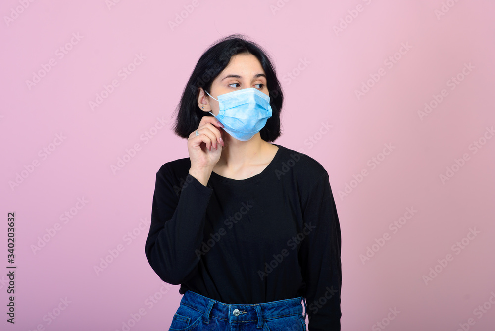 The caucasian girl in blue colored protective face mask. The girl looking at camera. Portrait shot over pink background. virus and pollution protection concept. The caucasian girl in blue colored protective face mask. The girl looking at camera. Portrait shot over pink background. virus and pollution protection concept.
