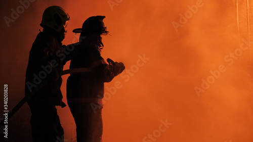 Rear view of Asian fireman wear fire protection suit. Firefighter spray water fighting. Emergency, Fire! at night..