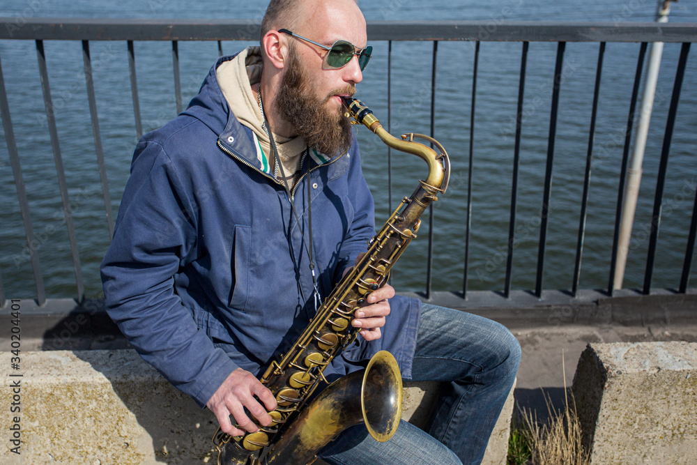 Fototapeta premium a handsome male saxophonist with glasses plays on the streets of the city