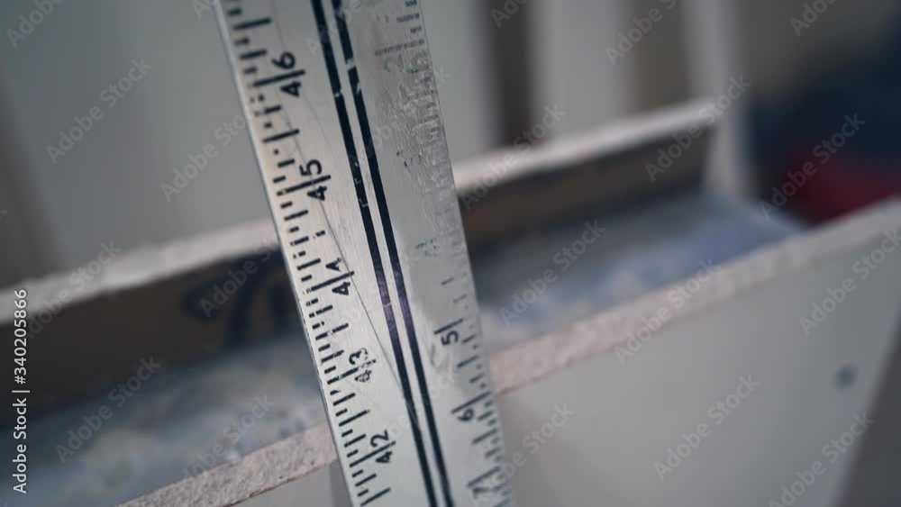 Tracking shot of long, worn metal ruler leaning on drywall in slow motion. Tracking shot of long, worn metal ruler leaning on drywall in slow motion.
