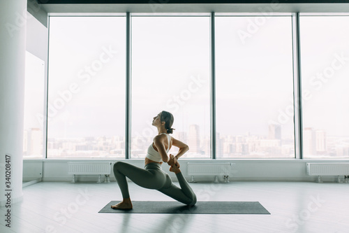  Stretching in the white room by the window. Beautiful girl athlete on the Mat. Flexibility exercises on a light background.