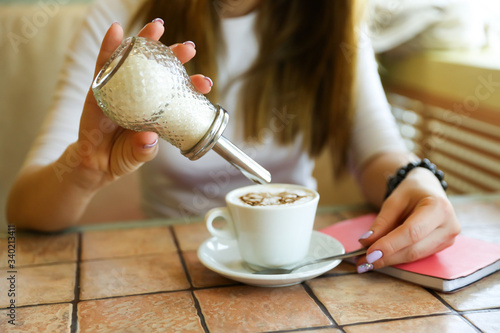 girl puts sugar in coffee from a sugar bowl dispenser photo