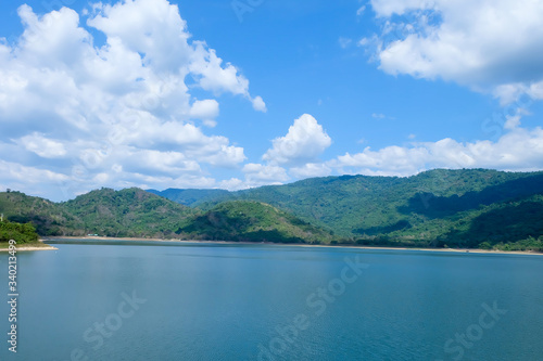The road beside the reservoir with mountains in the background, blue sky and white clouds