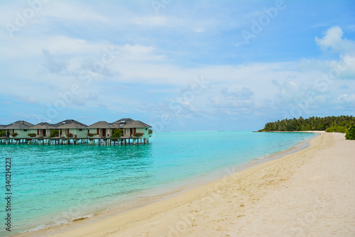 Fototapeta Naklejka Na Ścianę i Meble -  Bright sea beach with houses on the water, amid the rainforest and all this under a blue cloudy sky. photos on vacation. vacation at sea. tropical trees. palm trees. yellow and gray sand. sky horizon.