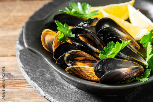 Cooked mussels in a black ceramic plate on a brown wooden table