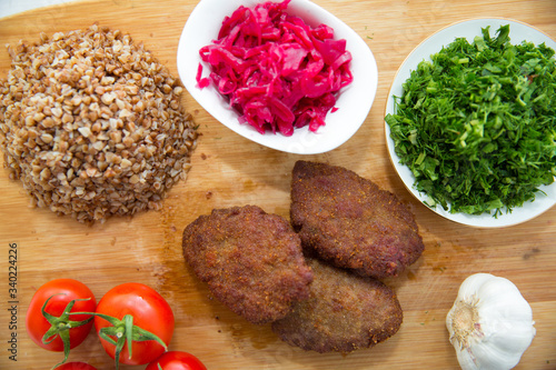 Meat cutlets, baked buckwheat on a wooden board . Red cabbage sauerkraut . Garlic, Onion, Tomatoes. Coriander. Homemade cutlets with oatmeal on a wooden table . Meat cutlets on a wooden skewer .