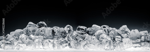 Heap of translucent crushed ice cubes on black background. Wide format.