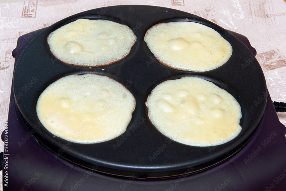 Close-up of the dough for four pancakes is cooked in an electric pan, top view Close-up of the dough for four pancakes is cooked in an electric pan, top view