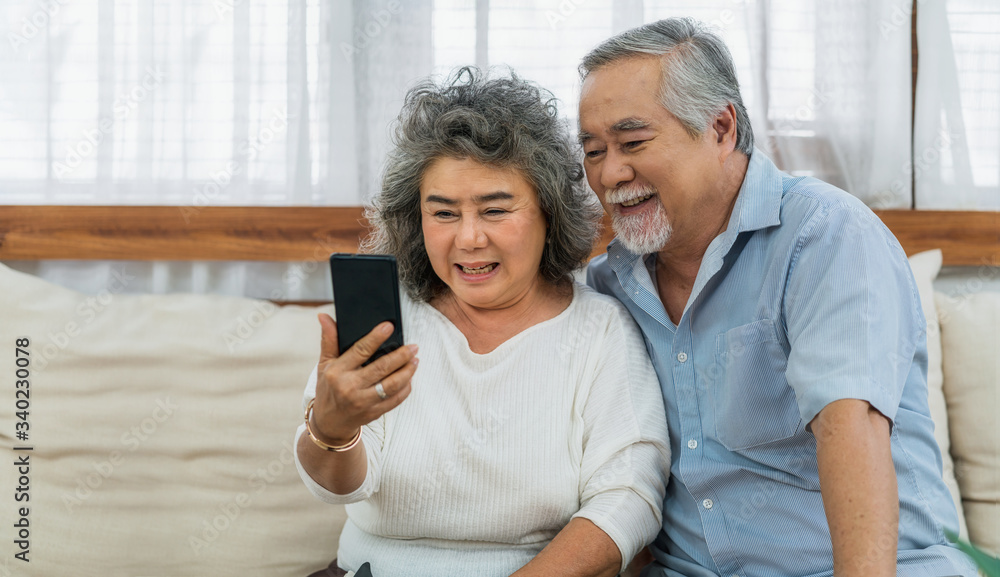 Asian couple Grandparent taking Video call to grandchild or taling selfie with happy feeling by mobile phone in house, Long live and Elderly society,Warm family and happiness,social distancing concept