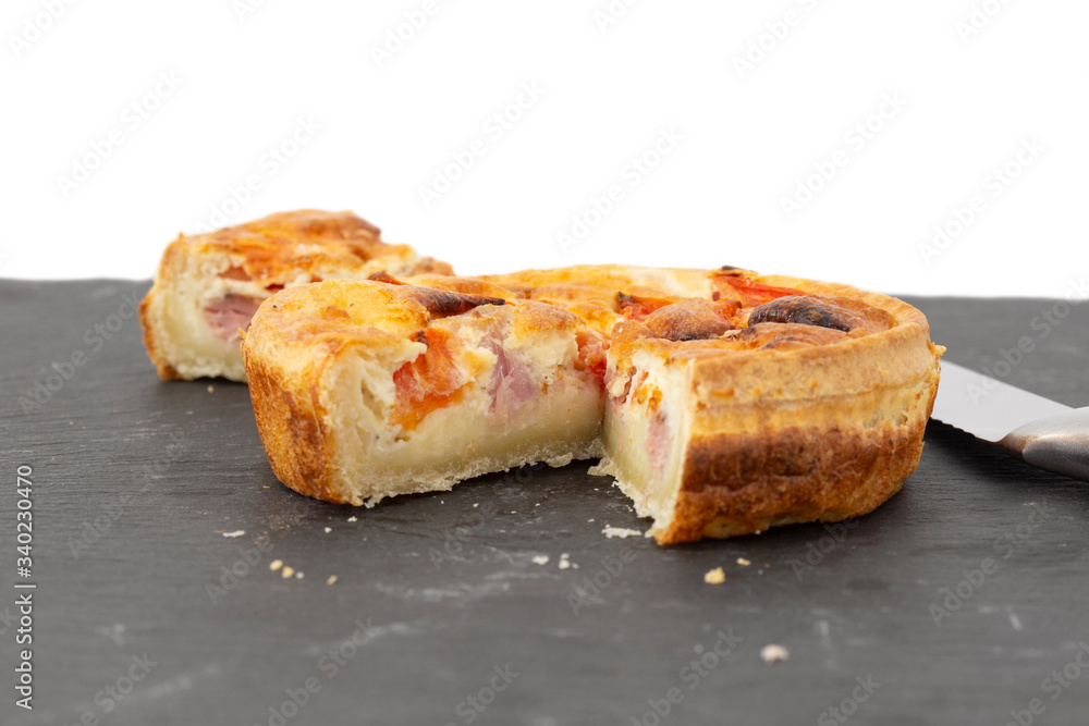 Ham and tomato quiche sliced with a knife. On a slate chopping board with a white background Ham and tomato quiche sliced with a knife. On a slate chopping board with a white background