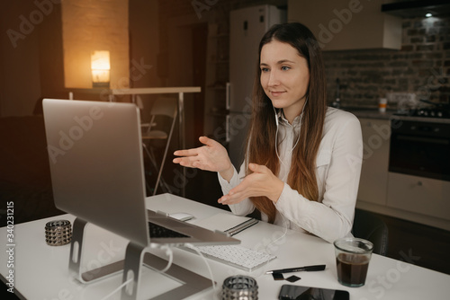 Remote work. A brunette woman with headphones working remotely online on her laptop. A girl actively discussing business with her colleagues through a video call at her cozy home workplace.