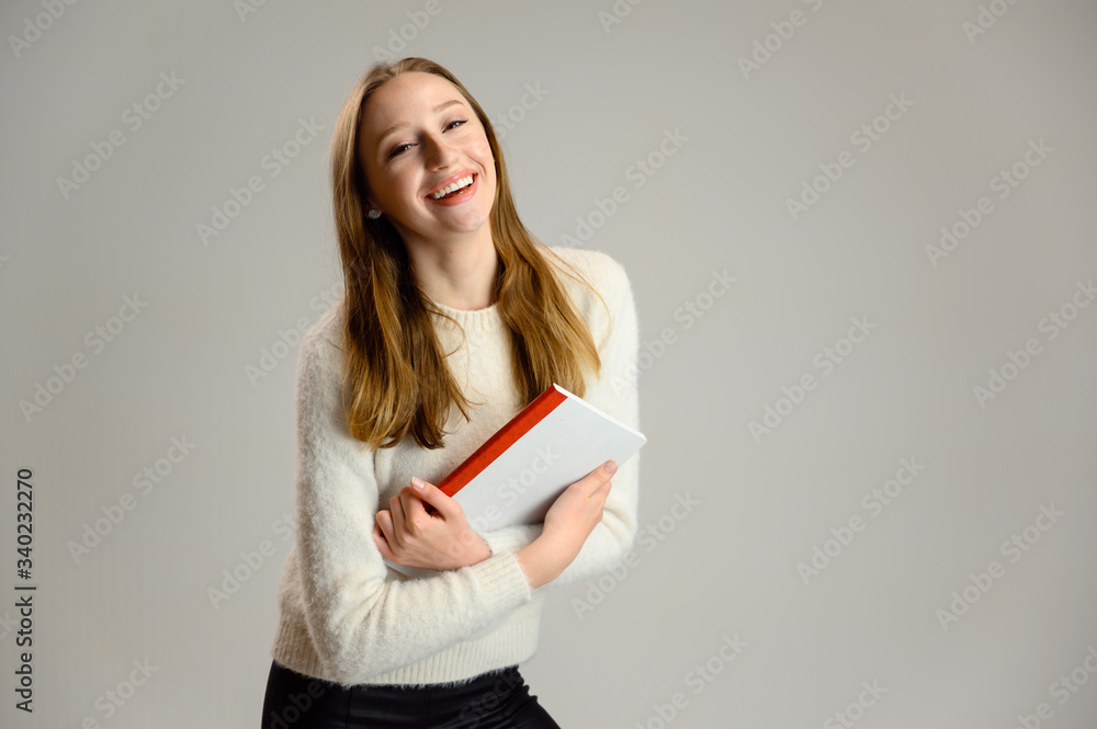Studio portrait of a happy caucasian female student girl with a smile in a white sweater on a white background with a folder in hands Studio portrait of a happy caucasian female student girl with a smile in a white sweater on a white background with a folder in hands