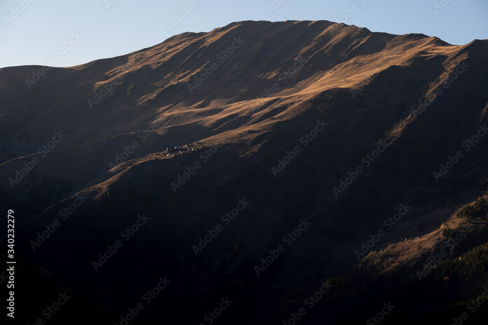 A village on a mountainside is lit by the setting sun in the Tusheti region.