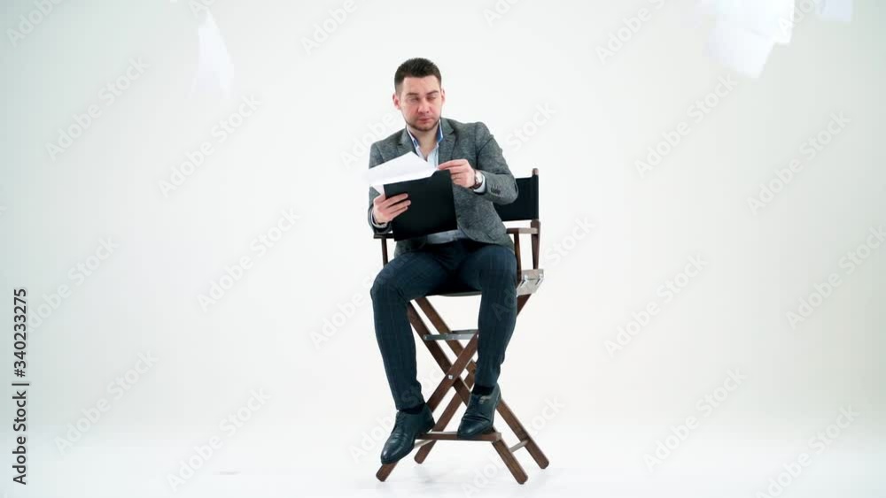 Elegant man with a folder. Businessman sitting on the chair and reading documents. Many papers are flying in the studio over the handsome man. Elegant man with a folder. Businessman sitting on the chair and reading documents. Many papers are flying in the studio over the handsome man.