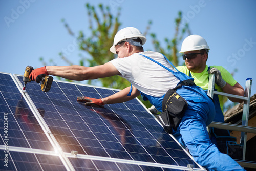 Two workers technicians connecting heavy solar photo voltaic panels to high steel platform. Exterior solar system installation, alternative renewable green energy generation concept.