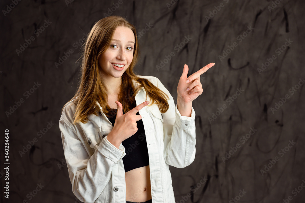 Fototapeta premium Studio photo of a happy caucasian girl in a white jacket stands in front of the camera on a gray background with a smile, showing hands