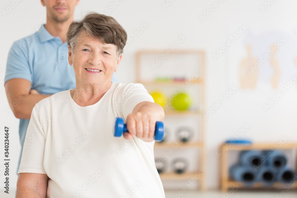 Smiling senior lifitng a weight during a rehabilitation Smiling senior lifitng a weight during a rehabilitation