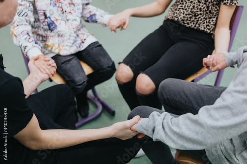Close-up of four people sitting together in a circle, holding hands © Photographee.eu