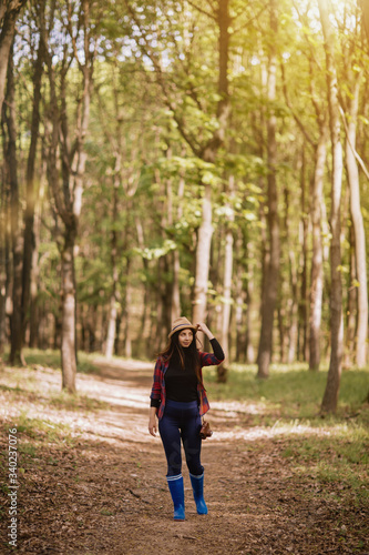 Stylish hipster young woman walking in the forest, carrying a backpack in the forest on sunset light in the spring season, looking at amazing woods, travel concept.