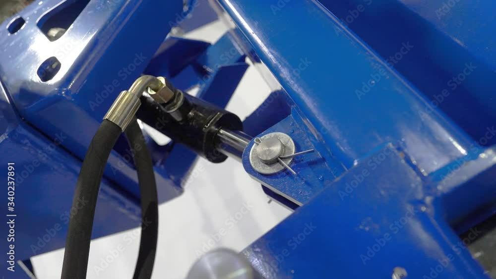 Operator on a blue tractor, excavator raises a bucket, a hitch, a mower