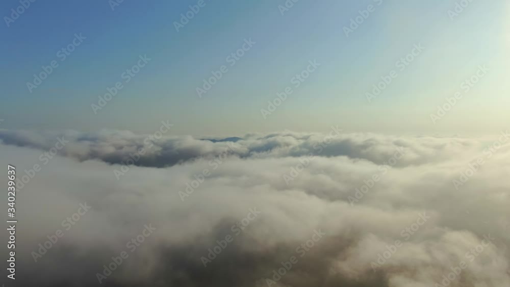 AERIAL movement over the thick fog lying on the ground from which only the mountain peaks of the Blue Sky are visible brightly illuminated by the sun AERIAL movement over the thick fog lying on the ground from which only the mountain peaks of the Blue Sky are visible brightly illuminated by the sun