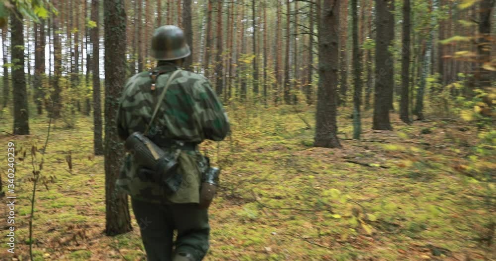 Historical Re-enactment. Re-enactor Dressed Like German Wehrmacht Infantry Soldier In World War II Marching Along Forest In Autumn Day. Group of Soldiers Marching In Forest Historical Re-enactment. Re-enactor Dressed Like German Wehrmacht Infantry Soldier In World War II Marching Along Forest In Autumn Day. Group of Soldiers Marching In Forest
