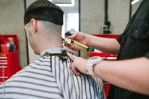 Male hairdresser trims client's hair with golden trimmer, close up photo. A professional barber creates a fashionable hairstyle for a man with dark hair in a barber shop using a trimmer.