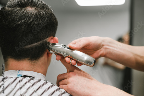 Barber cuts the back of his head with a clipper in his hand. Professional male hairdresser does hairstyle for client in barbershop, close-up photo process. Copy space