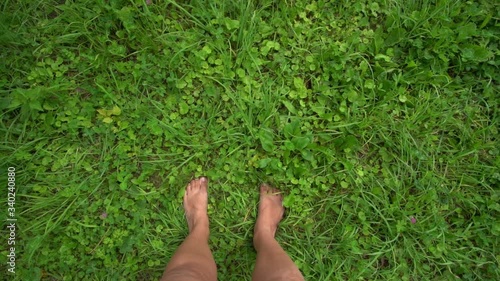 Closeup top view video of beautiful naked female legs walking on fresh delicate green wild grass with different plants growing in meadow in countryside. Point of view shooting from first person.