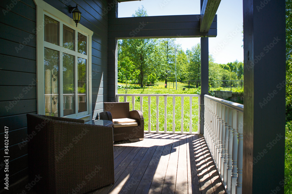 View from the terrace of a country wooden house to the garden through the white wooden railing of the terrace. Verandah of a house in a Park in summer among trees and bushes View from the terrace of a country wooden house to the garden through the white wooden railing of the terrace. Verandah of a house in a Park in summer among trees and bushes
