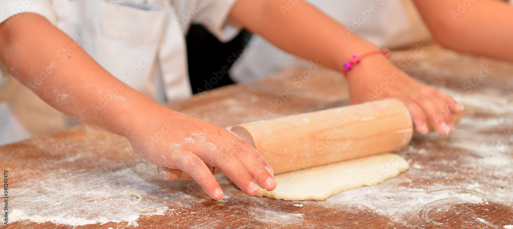 Little kids make dough products. Flour is scattered around. Hands close up.