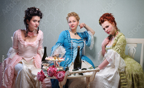 Three beautiful ladies in lavish dresses at a party in a historical setting photo