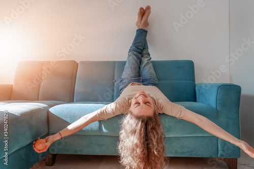 Portrait of  lovely  cheerful cheery curly girl having fun lying on blue sofa with head upside down, happy and free lifestyle concept