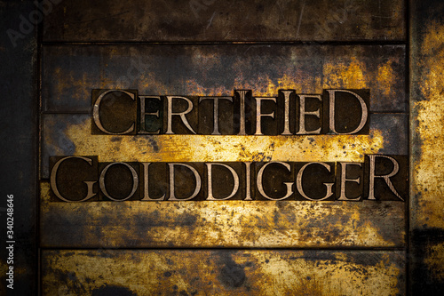 Photo of real authentic typeset letters forming Certified Golddigger text on vintage textured grunge copper and gold background photo