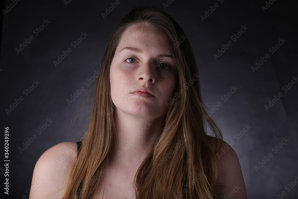 Fototapeta premium Studio portrait of young girl with light hair and freckles, with dark background.