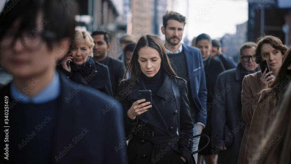 Beautiful Businesswoman in Black Coat is Using a Smartphone on a Street in Downtown. She Walks on a Crowded Pedestrian Street and Looks Successful. She's Browsing the Web on Her Device. Beautiful Businesswoman in Black Coat is Using a Smartphone on a Street in Downtown. She Walks on a Crowded Pedestrian Street and Looks Successful. She's Browsing the Web on Her Device.