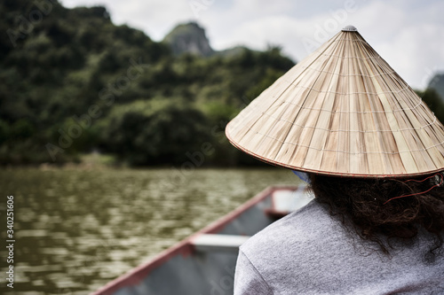 young adult in a boat  watching the birds in a natural park  with typical Vietnamese hat 