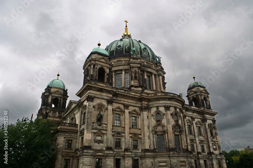 View of the upper part of the cupola of the Berlin Cathedral with the turquoise copper roof and golden cross on top in front of an impressive sky with white grey clouds; Berlin, Germany, Europe 
