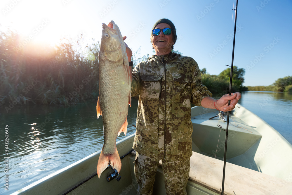 Happy fisherman holds trophy Asp fish being in the boat on a lake Happy fisherman holds trophy Asp fish being in the boat on a lake