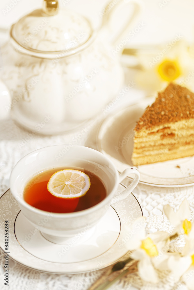Closeup slice of lemon in a cup of tea on a background of flowers and a teapot