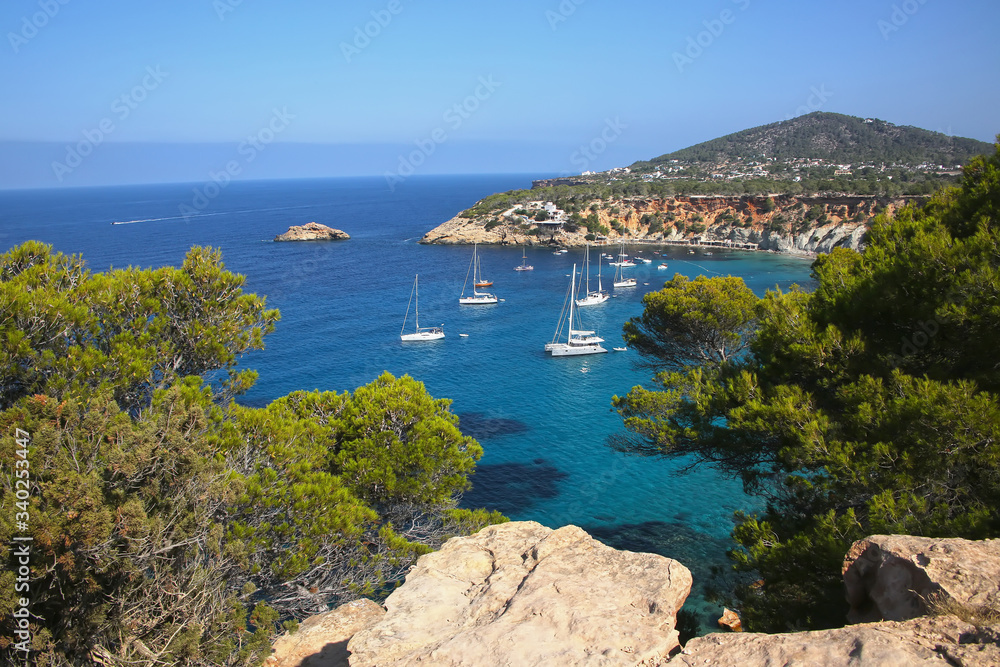 View from the South coast of Ibiza showing boats anchored in the bay. Beautiful landscape with cliffs & turquoise water. Baleric Islands, Spain.