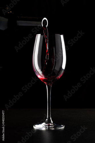 Red wine being poured into a glass and splashing over the side. Low key black background.